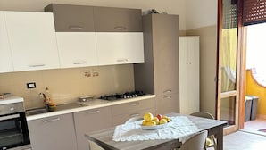 Una cocina moderna con armarios blancos, una estufa a gas y una mesa de comedor con cojines amarillos.