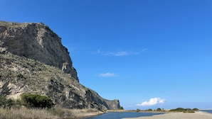Un paisaje costero con una playa de arena, un río y un acantilado rocoso.