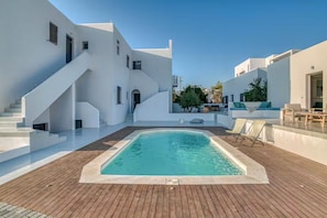 A modern pool area with a wooden deck, white walls, and a staircase leading to an upper level.