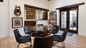 A modern dining area with a glass-top table surrounded by chairs, a mounted animal head, and a stone wall.