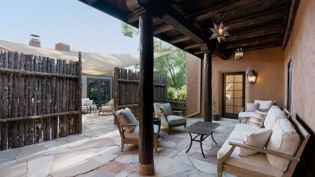 An outdoor patio with stone flooring, wooden furniture, and a wooden pergola.