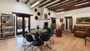 A spacious living room with a glass-top dining table, modern furniture, a fireplace, and a large painting on the wall.