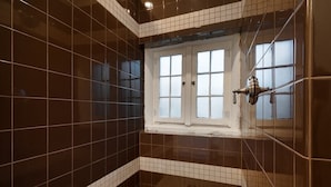 A bathroom with dark brown tiles, a window with frosted glass, and a metal towel rack.