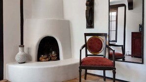 Una habitación con chimenea, una silla, un espejo y una pared blanca.