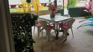 Un patio couvert avec une table et des chaises, entouré de plantes en pot et offrant une vue sur un bâtiment en arrière-plan.