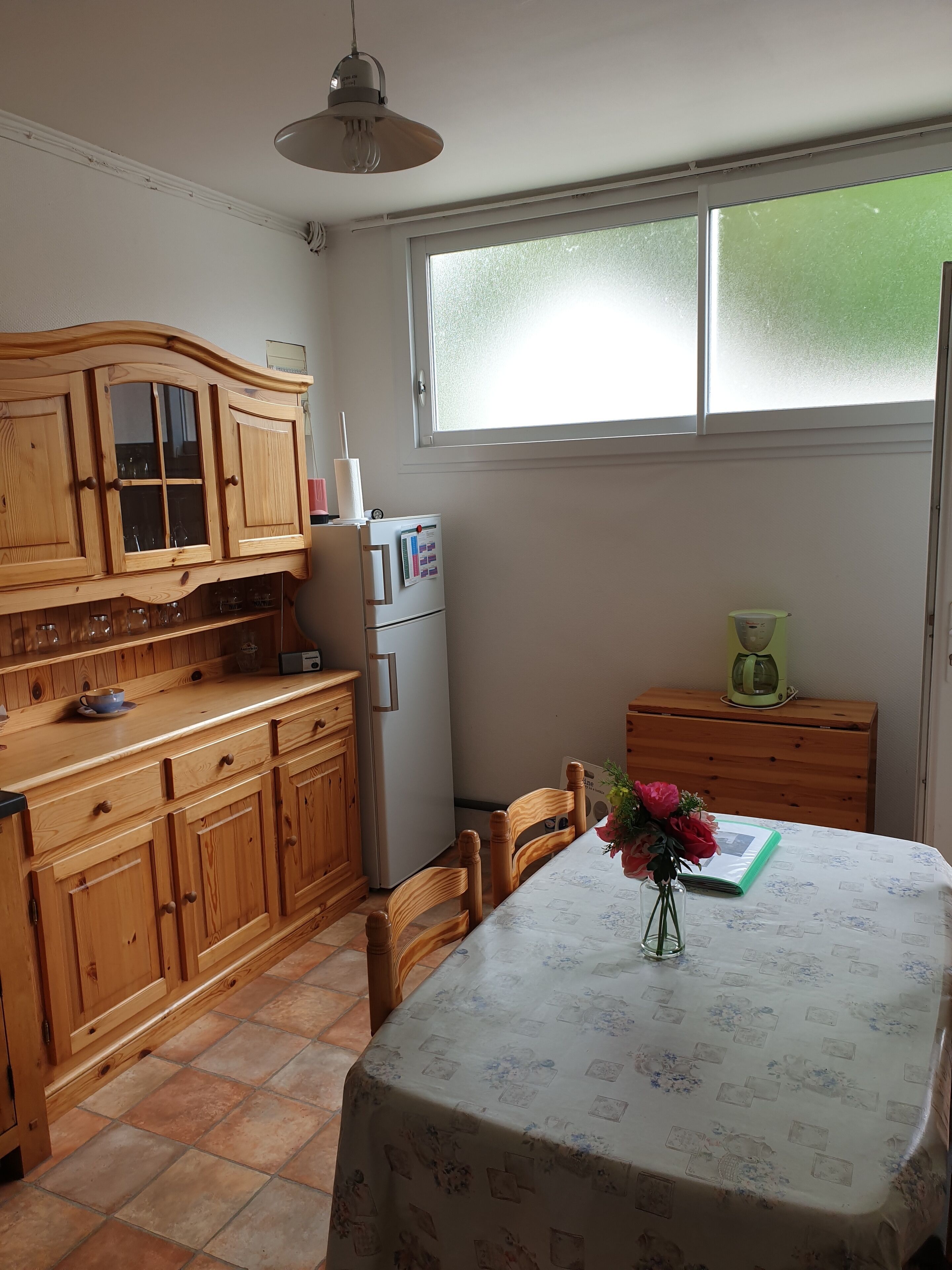 Una cocina con armarios de madera, un refrigerador, una mesa de comedor con sillas y un ventanal con vidrio esmerilado.