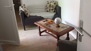 Un salon avec un canapé, une petite table sur laquelle se trouvent un globe terrestre et un jeu de société, une porte et un couloir menant à une salle de bain.
