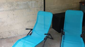 Two turquoise lounge chairs with black metal frames, positioned on a tiled patio against a beige brick wall.
