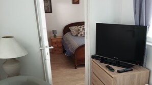 Une pièce comprenant un lit, un téléviseur posé sur un meuble en bois, une lampe et une chaise.