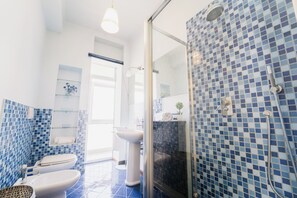 A modern bathroom with blue mosaic tiles, a glass shower enclosure, a white sink, and a toilet. - Elegant Apartment in the Center by Wonderful Italy (Sanremo)