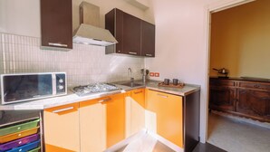 A compact kitchen with a microwave, gas stove, and wooden cabinets. - Elegant Apartment in the Center by Wonderful Italy (Sanremo)