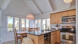 Una cocina con armarios de madera, horno de acero inoxidable, lavavajillas y un amplio ventanal que proporciona luz natural.