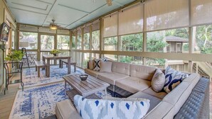 A covered patio with a wooden ceiling, large windows, a sofa, a table, and a dining area. - Seabrook Exclusives | 1138 Summerwind (Johns Island)