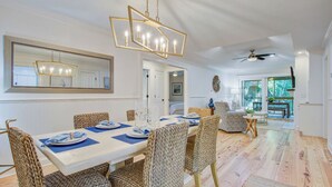 A dining area with a long table, woven chairs, and a chandelier. - Seabrook Exclusives | 1138 Summerwind (Johns Island)