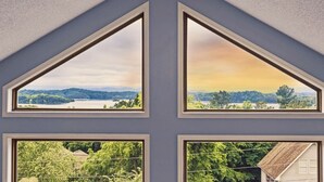 Una habitación con cuatro ventanas, cada una con una vista distinta: un lago, un bosque, una zona residencial y una línea eléctrica.