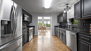 Una cocina moderna con electrodomésticos de acero inoxidable, armarios oscuros y un amplio ventanal con vistas a un comedor.