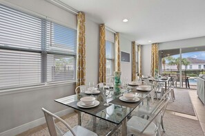 A dining area with a glass table, white chairs, and a view of the outdoors.