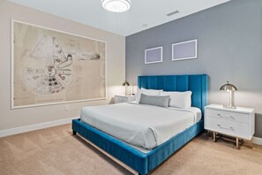 A bedroom with a large bed, a blue headboard, two bedside tables, and a wall-mounted artwork of a spacecraft.
