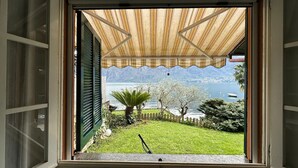 Janela com vista para um jardim, um lago e montanhas.