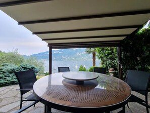 Ein runder Tisch mit Lochglasplatte, umgeben von vier Stühlen, unter einer Pergola mit Blick auf einen See und Berge.