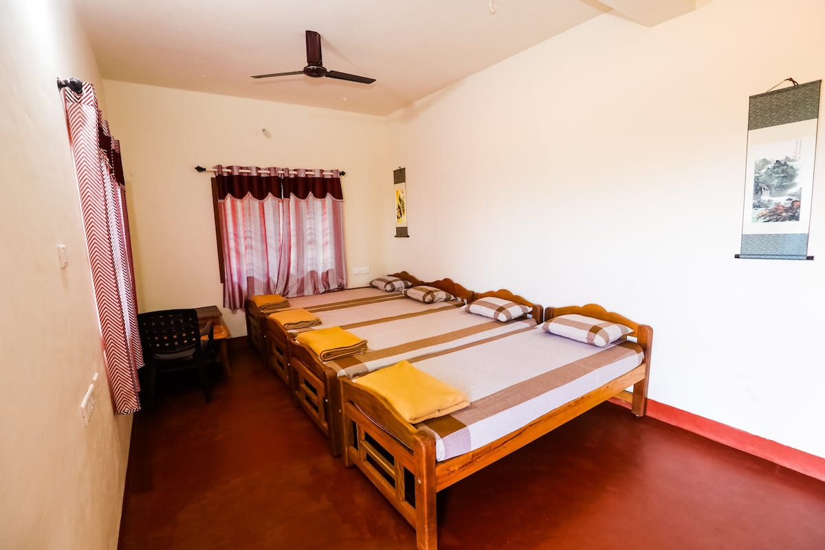 Ein Zimmer mit einem großen Bett, einem Deckenventilator, einem kleinen Tisch mit Stuhl und einem Wandbild.
