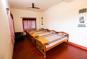 A room with a large bed, a ceiling fan, a small table with a chair, and a wall-mounted artwork. - Uttunga Homestay (Mudigere)