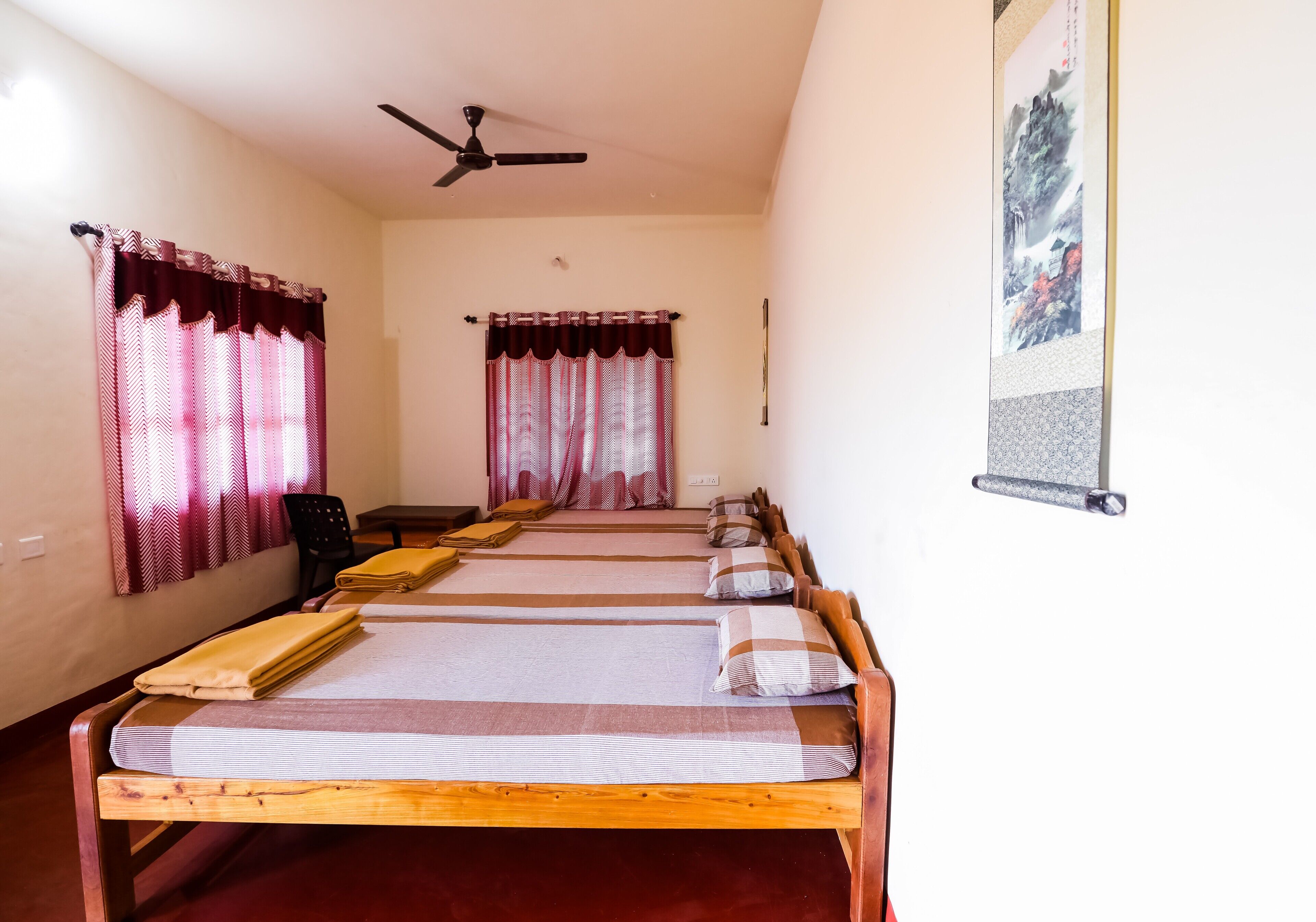 A room with four single beds, a ceiling fan, and a wall-mounted poster.