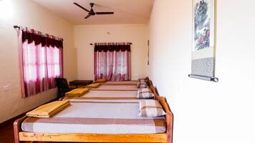 A room with four single beds, a ceiling fan, and a wall-mounted poster.