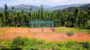 A tennis court surrounded by lush greenery and mountains in the background. - Uttunga Homestay (Mudigere)