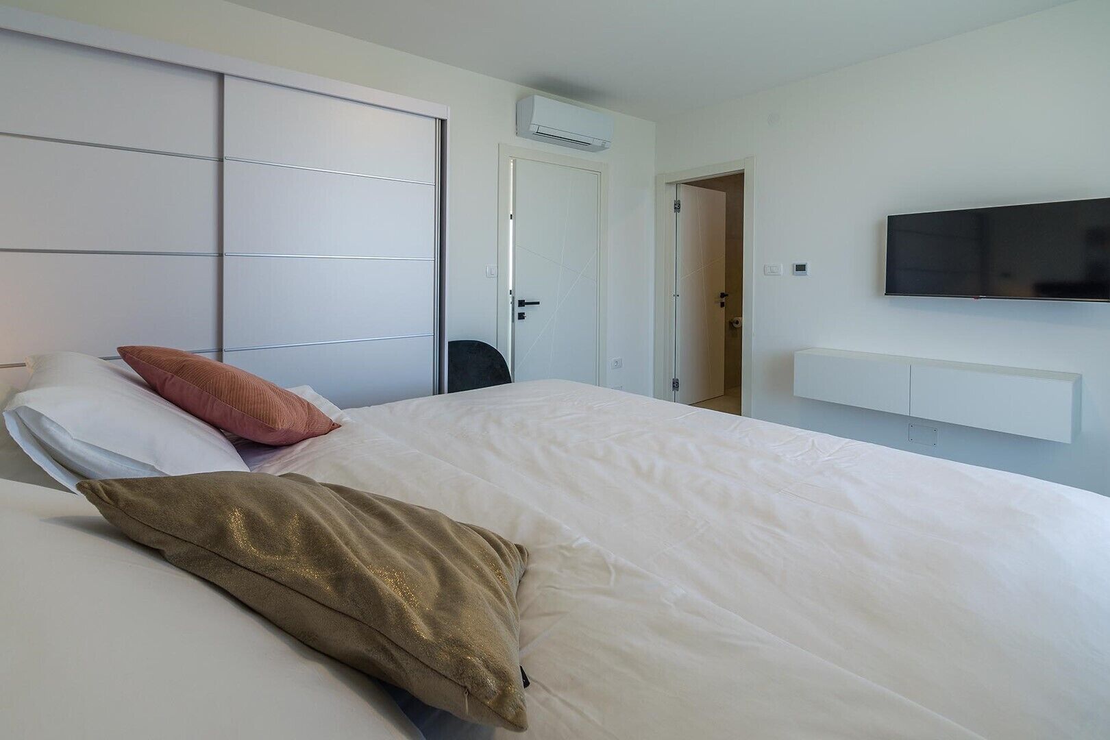 A hotel room with a bed, a TV mounted on the wall, and a wardrobe with sliding doors.