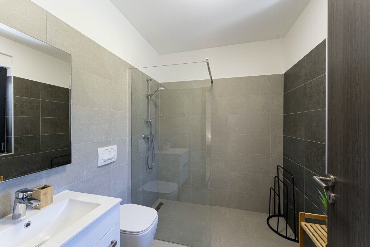 A modern bathroom with a glass-enclosed shower, a white sink, and a toilet.