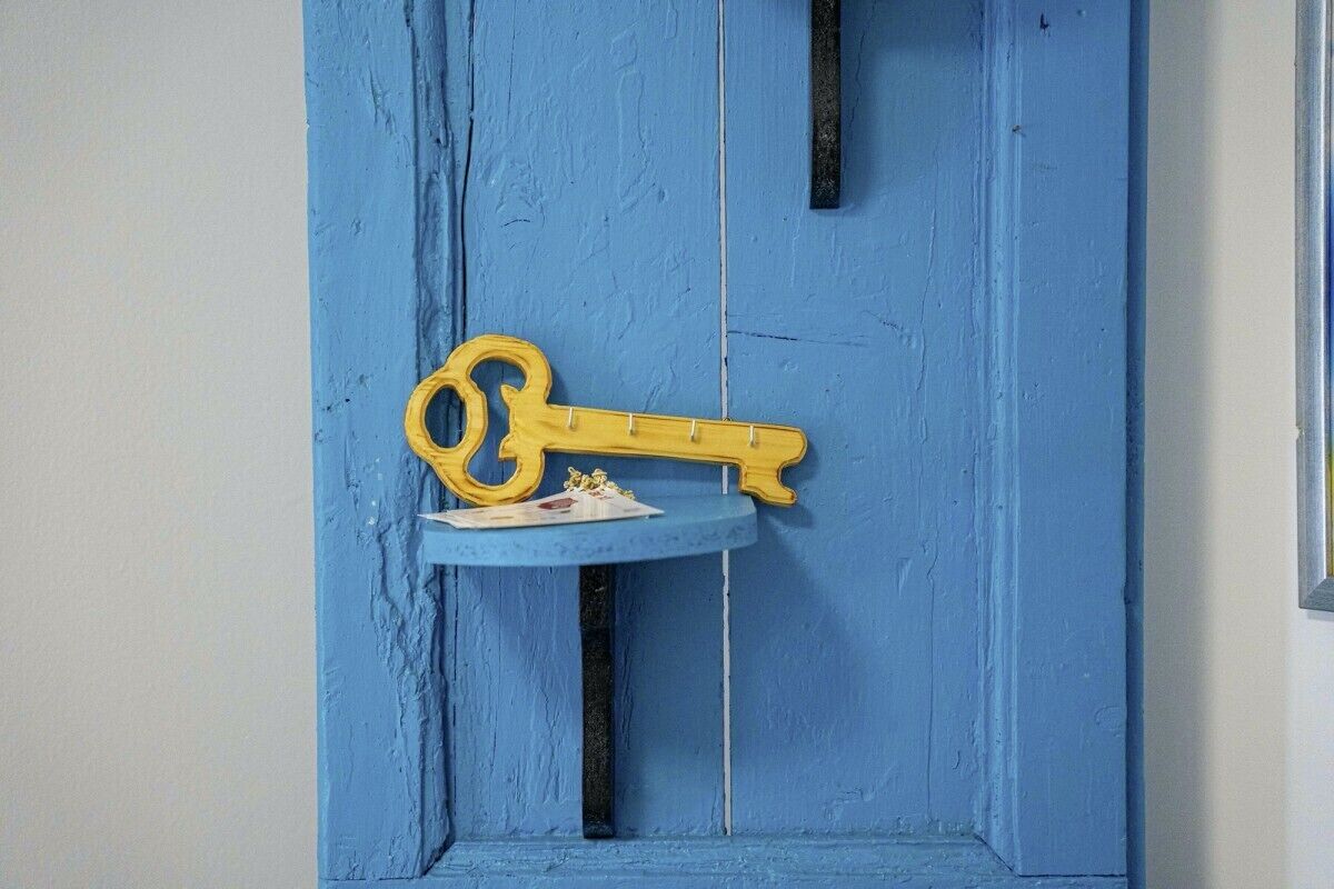 A blue door with a yellow key hanging on a small shelf.