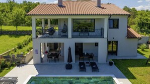 A two-story house with a swimming pool, outdoor seating, and a garden.