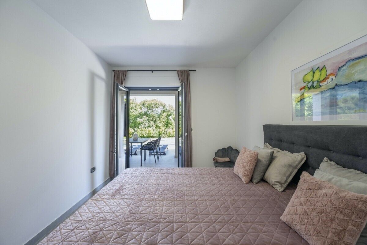 A bedroom with a large bed, a headboard, and a view of an outdoor patio.