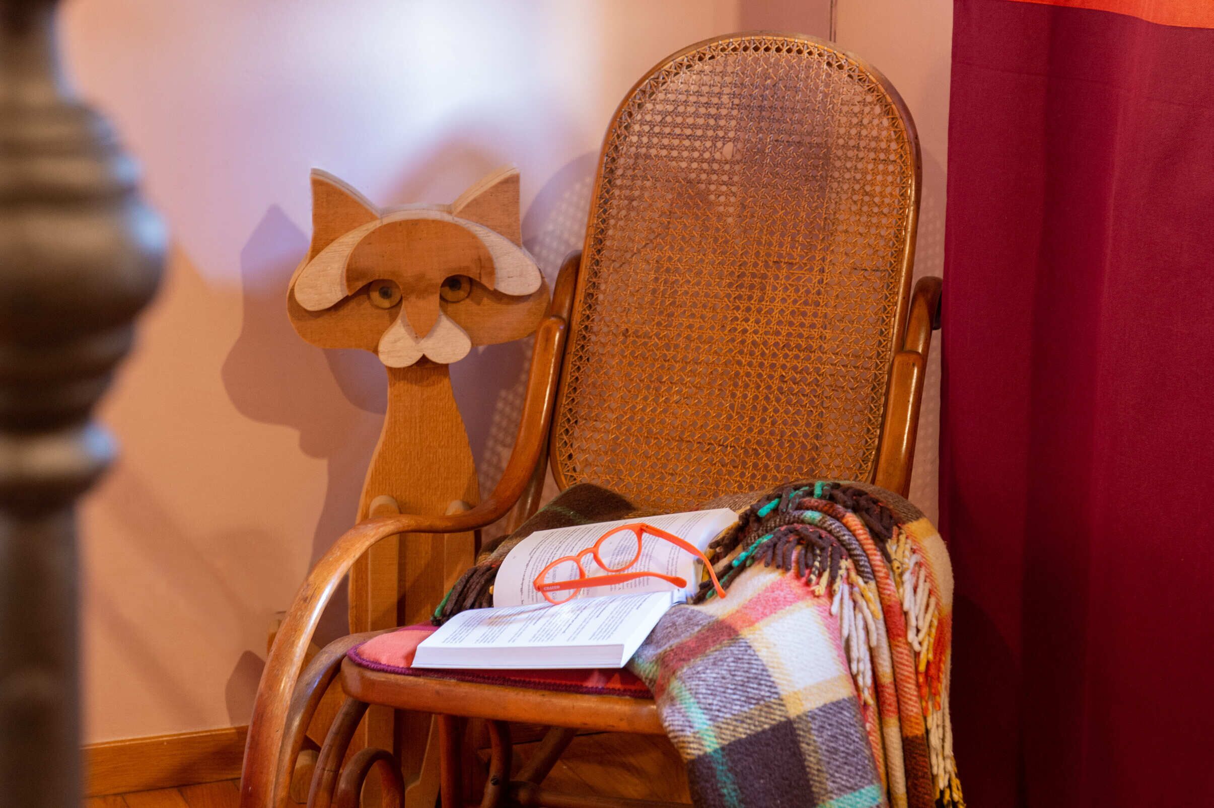 Une chaise en bois avec un dossier en osier tressé, un coussin décoratif en forme de renard, un livre et une couverture colorée.