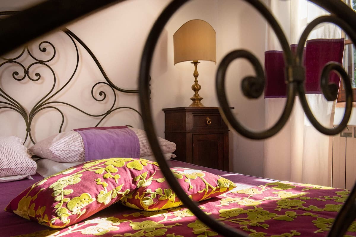 Un lit avec une couvre-lit à motifs et des coussins décoratifs, une lampe de chevet et une table de chevet en bois.