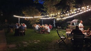 An outdoor gathering with string lights and tables, surrounded by trees.