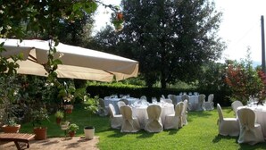 An outdoor garden setting with round tables and chairs, a large umbrella, and potted plants.