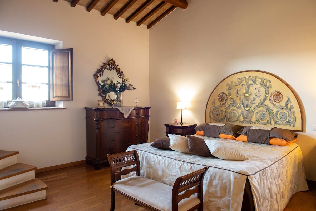 Une chambre à coucher avec un lit, une chaise, une commode, un miroir et une fenêtre.