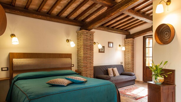 A bedroom with a large bed, a sofa, and a small cabinet with a plant.