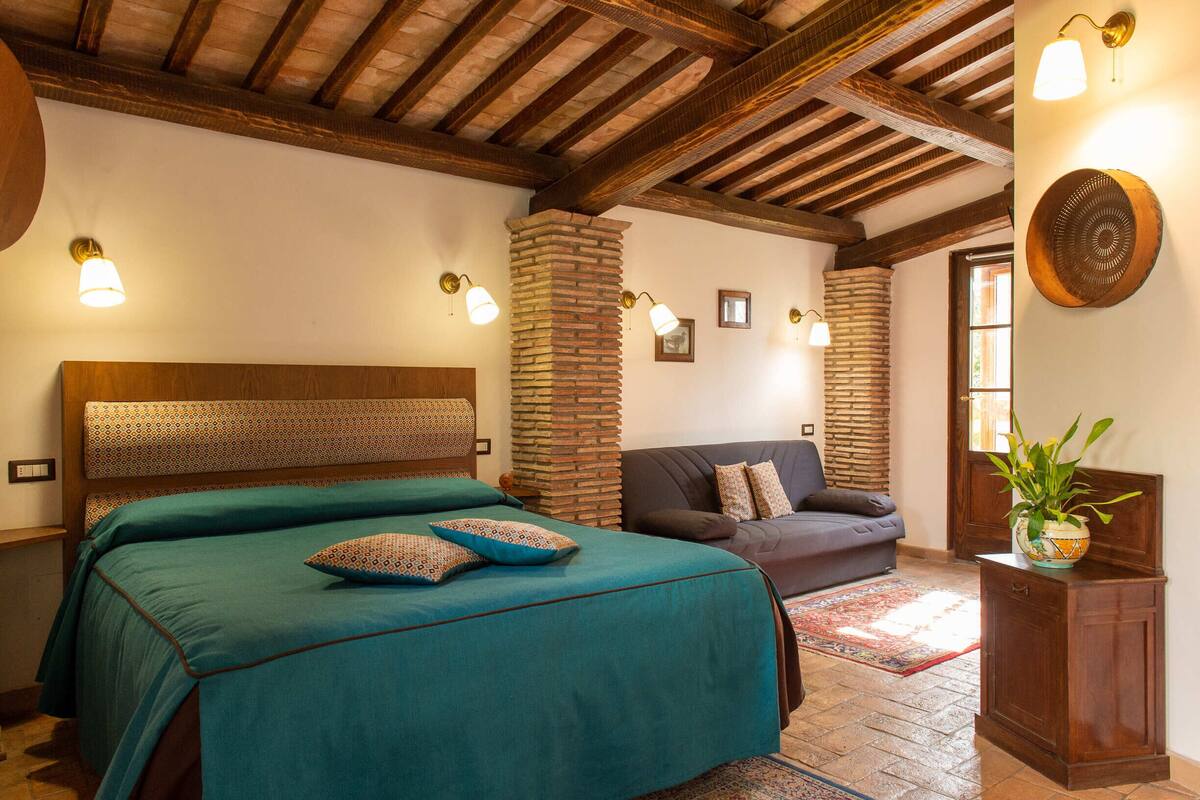 Une chambre à coucher avec un grand lit, un canapé et une petite armoire sur laquelle est posée une plante.