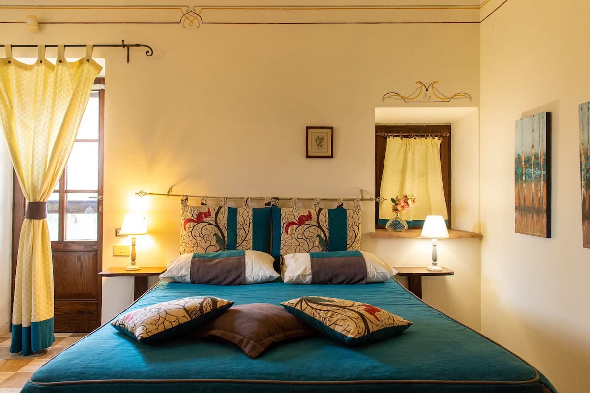 Une chambre à coucher avec un lit, deux lampes de chevet, une fenêtre avec des rideaux et un tableau encadré au mur.