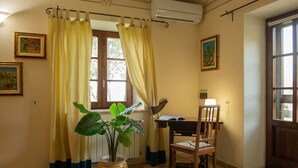 A room with a checkered floor, a potted plant, a chair, a desk with a lamp, and two windows with curtains.