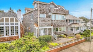 A two-story house with a prominent front porch, a chimney, and a well-maintained garden. - Beautiful multi-level oceanfront home, perfect retreat for friends or family. (Seaside)