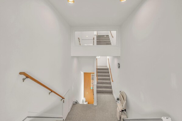 A modern interior with a staircase leading to an upper level, white walls, and a carpeted floor. - Beautiful multi-level oceanfront home, perfect retreat for friends or family. (Seaside)