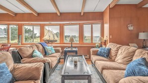 A cozy living room with wooden walls and large windows, a comfortable sofa set, and a coffee table. - Beautiful multi-level oceanfront home, perfect retreat for friends or family. (Seaside)