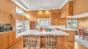A modern kitchen with wooden cabinets, stainless steel appliances, and a central island with bar stools. - Beautiful multi-level oceanfront home, perfect retreat for friends or family. (Seaside)
