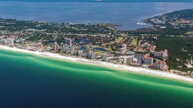An aerial view of a coastal resort with multiple high-rise buildings, a beachfront, and a large body of water. - Summit 0407 (Miramar Beach)