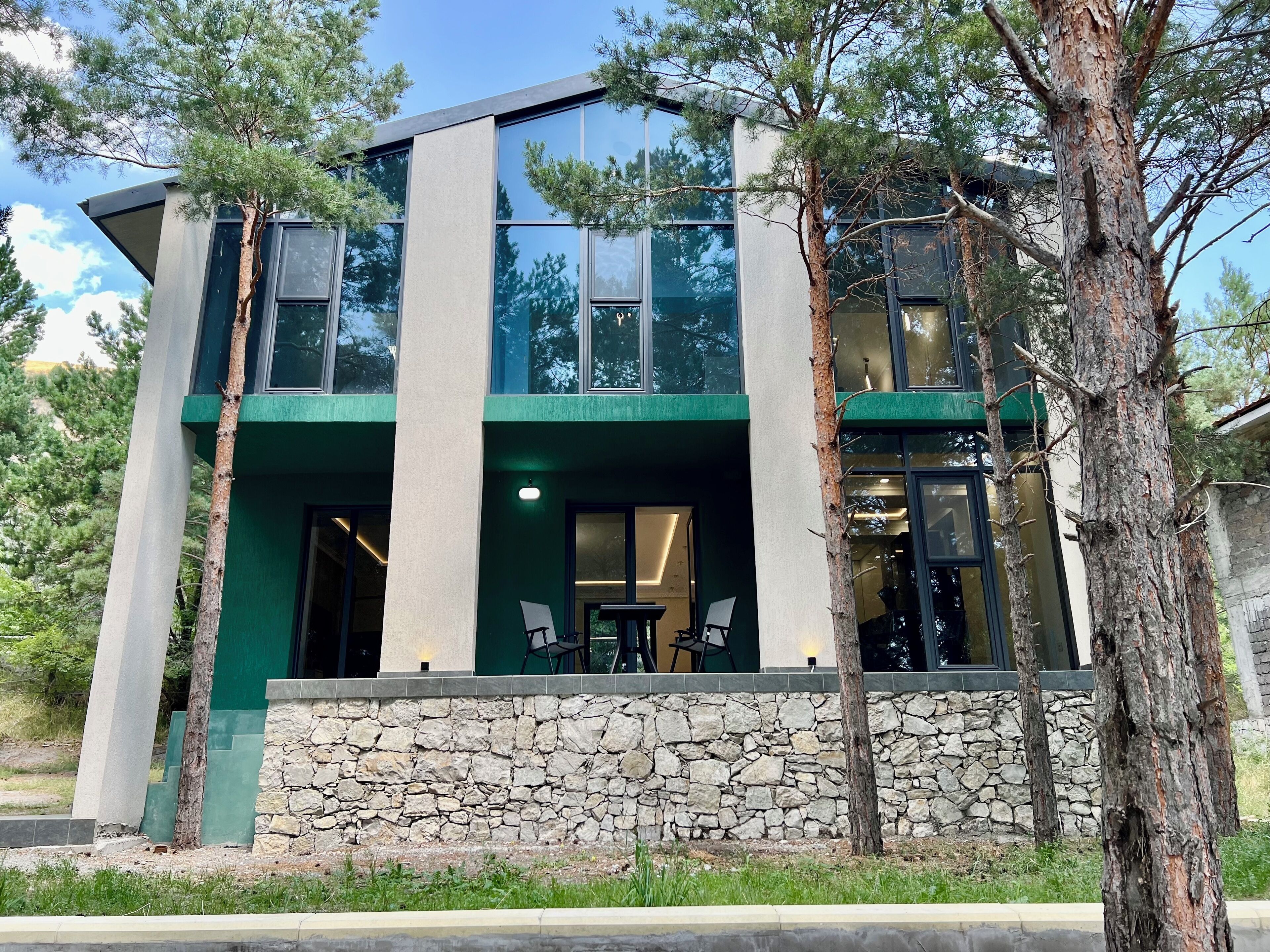 Une maison moderne à deux étages, dotée de fondations en pierre, de grandes fenêtres et d’un mur d’accent de couleur verte.