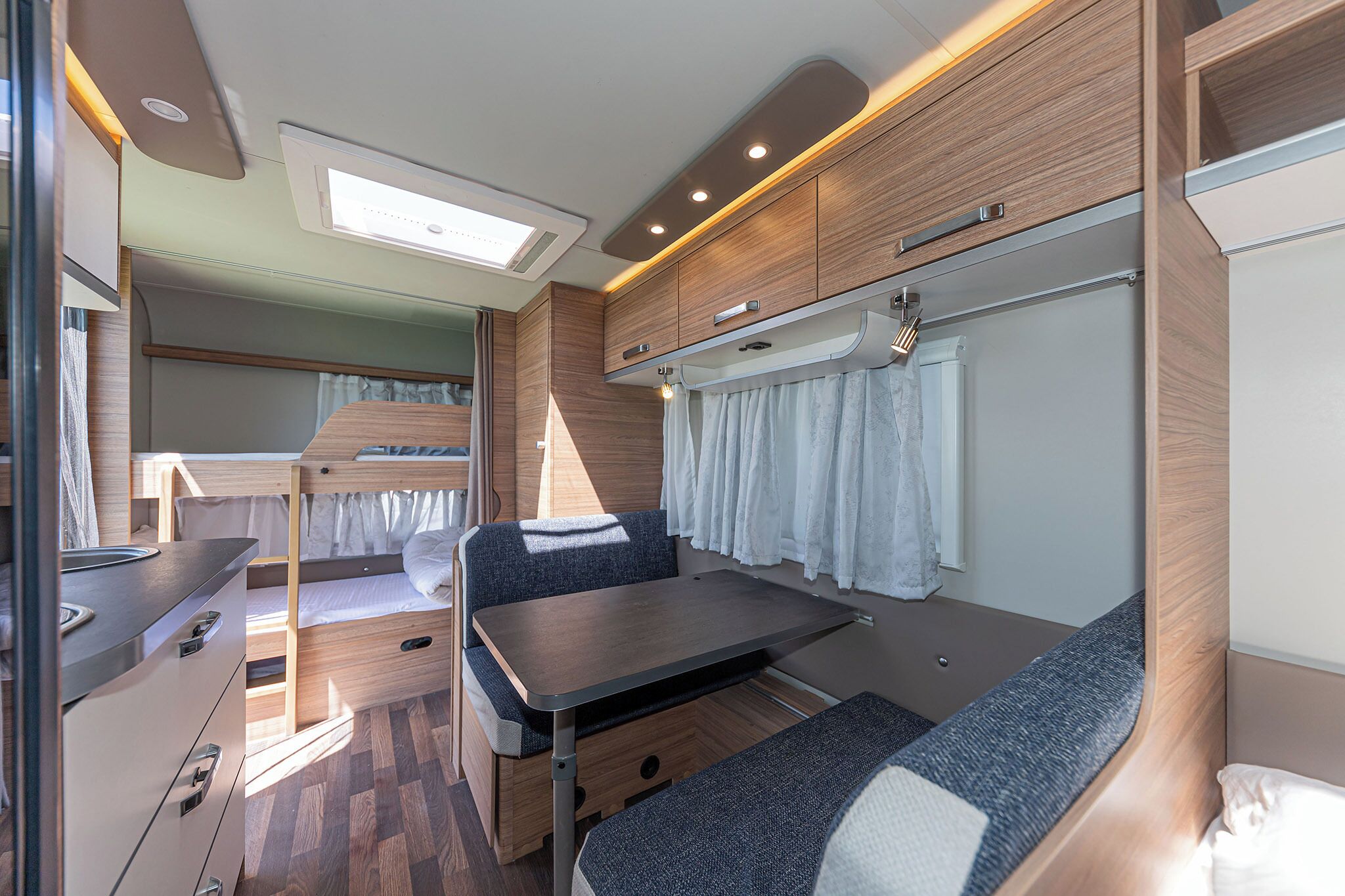 A compact RV interior with a kitchenette, a dining area, and a sleeping berth.